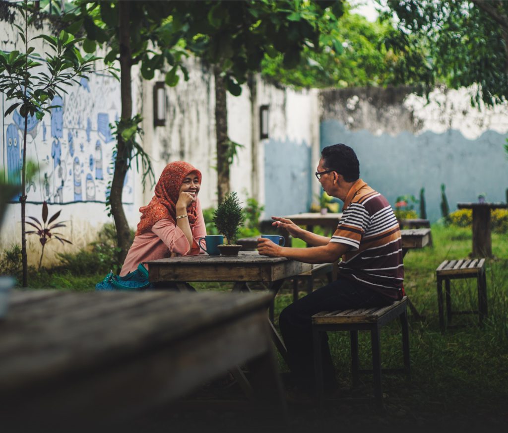 Middle aged south asian man and woman in a Tudong scarf discussing happily at a table outdoors